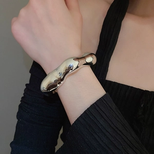 Detail view of a chunky irregular silver liquid metal wave bangle on a model's wrist
