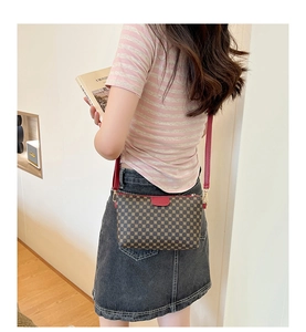Detail of a brown patterned crossbody bag with red trim worn by a model in a modern room