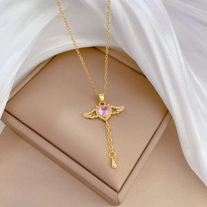 Detail of gold wing necklace with pink heart gemstone on beige jewelry box