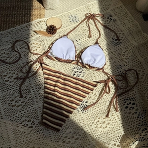 Piatto di un bikini a righe con pigne naturali su un tessuto di pizzo beige