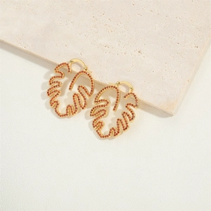 Exquisite gold monstera leaf earrings with red rhinestones on a white stone background