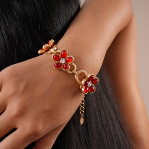 Elegant gold chain bracelet featuring red flower charms with sparkling diamond centers