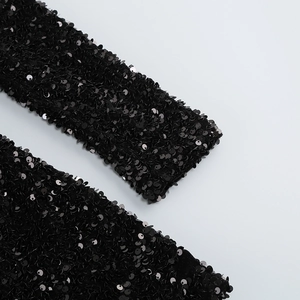 Gros plan des paillettes noires denses cousues sur la manche d'une robe de soirée
