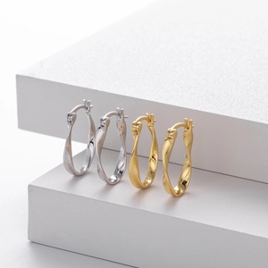 Macro view of minimalist twisted metal hoop earrings in gold and silver finish on a pedestal