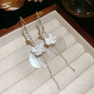 Elegant floral drop earrings with silver tassels and shell charms on beige velvet display