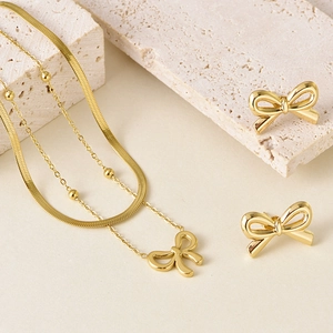 Ensemble collier double rangée et boucles d'oreilles nœud doré sur fond en pierre