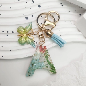 Close-up of resin letter A keychain with dried flowers, gold leaf, and butterfly charm