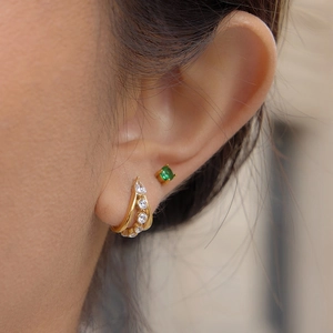 Close-up of a double-layer golden C-shaped earring with zircon and a green gemstone stud