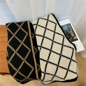 Detailed close-up of soft black and white checkered knit scarf on a cozy wooden table