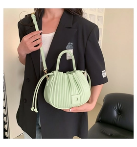 Detail view of mint green pleated PU handbag worn by a model in a minimalist urban setting