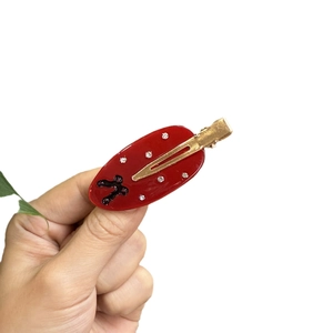 Elegant red resin hair clip with white rhinestones and black cross on gold metal base