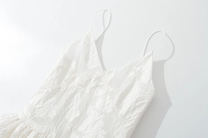 Detail of white V-neck dress featuring delicate floral jacquard texture and thin straps