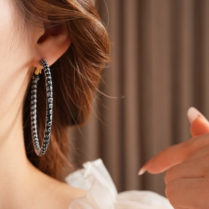 Detail of round hoop earring with black and white woven pattern on female model