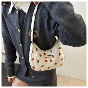 Close-up of white corduroy underarm bag featuring red strawberry prints and metal buckle