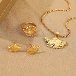 Flat lay of golden ginkgo leaf necklace, ring and earrings set on beige silk fabric