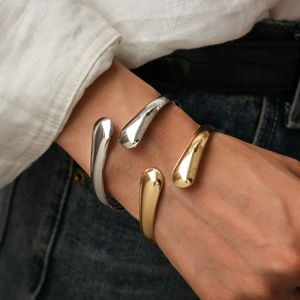 Detail of minimalist gold and silver open cuff bracelets with polished teardrop ends
