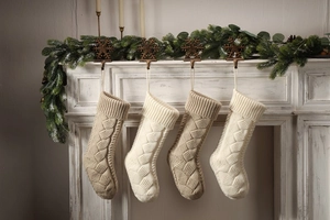Detail of four cable knit Christmas stockings in beige and ivory on a white fireplace