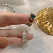 Dettaglio di anelli con zirconi arcobaleno e bianchi tenuti sulle dita
