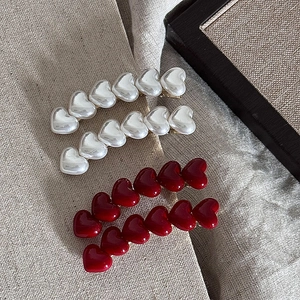 Detail of elegant red heart hair clips and pearl style barrettes on linen fabric