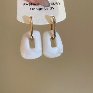 Detail of square white acrylic drop earrings with gold hoops on a white display card