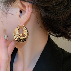 Close-up of golden chunky hoop earrings with geometric mesh texture worn by a model