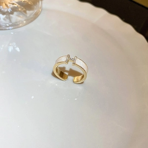 Close-up of golden H-shaped ring with white enamel and sparkling zircon diamonds