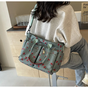 Detail of green tote bag with red cherry print featuring multiple zipper pockets