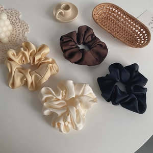 Detail of four satin silk scrunchies in black, brown, champagne, and cream white colors