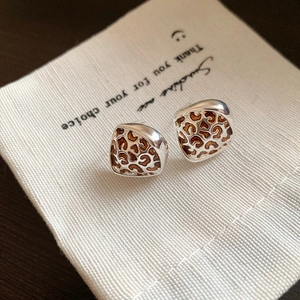 Close-up of leopard print heart earrings with silver metal frame on linen bag