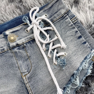 Dettaglio di pantaloncini di denim a vita alta con lacci e orli sfrangiati su tappeto