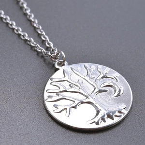 Macro shot of polished silver tree of life pendant on a fine stainless steel chain