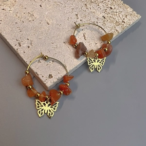 Detail of bohemian gold hoop earrings with natural orange stones and butterfly charm