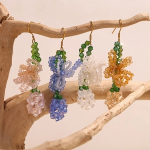 Close-up of handmade beaded floral earrings in pink, blue, and amber on wooden branches