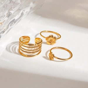 Three-piece gold stainless steel flower rings set with beaded layers on a wavy glass background