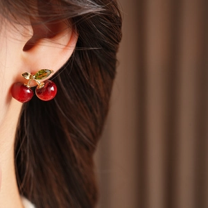 Close-up of red resin cherry earrings with golden stem and green crystal leaf detail