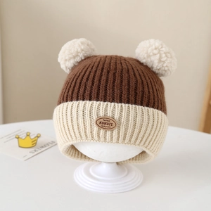Close-up of knit winter hat featuring two cream pom-poms and a round leather logo tag