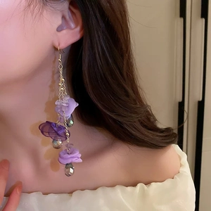 Close-up of purple fabric flower earrings with pearls worn by a model in soft light