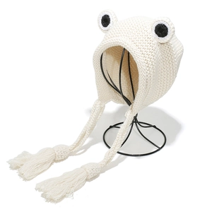 Detail view of white knit frog hat featuring thick woven cords and decorative tassels