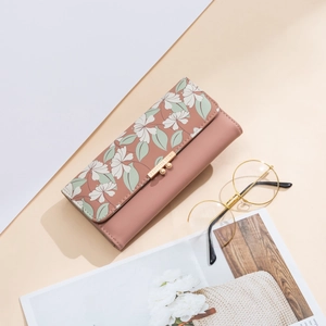 Close-up of pink long wallet with floral flap and golden metal buckle on a beige background