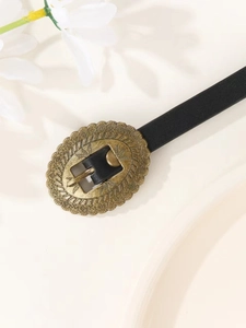 Close-up of vintage bronze buckle with floral engraving on a black PU leather belt