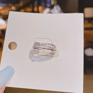 Detail of silver double-layer cross ring with zircons on white display card