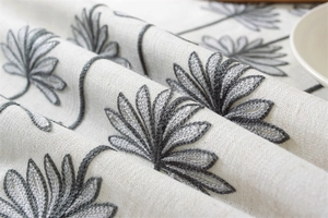 Detailed macro view of gray floral embroidery on cream linen waterproof tablecloth