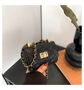 Detail of black quilted mini bag with gold twist lock and chain strap held by hand