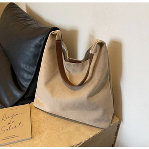 Detail of beige faux suede tote bag with brown leather strap on stone surface