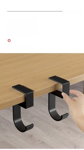 Adjustable black matte metal desk side hook for bags shown being installed on a wooden table