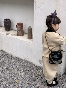 Nahaufnahme von beigem Kinderstrickoutfit mit schwarzer Leder-Mini-Umhängetasche