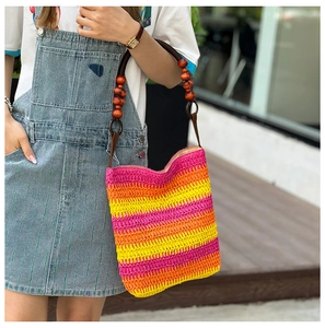 Detail of rainbow straw woven handbag featuring stylish brown wooden bead handles