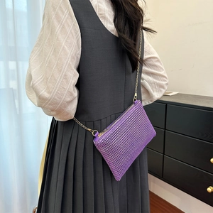 Detail of purple sequin envelope bag with gold chain strap on a model's shoulder