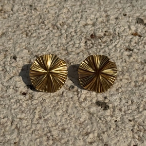 Macro detail of gold round earrings with sunburst texture on a stone background