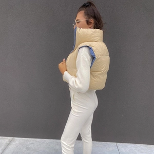 Side view of beige quilted cropped vest with stand collar on model against gray wall